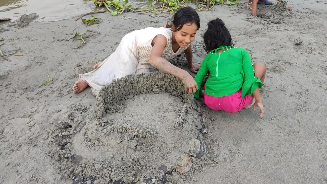 How the baby girls are playing with sand on the river side?